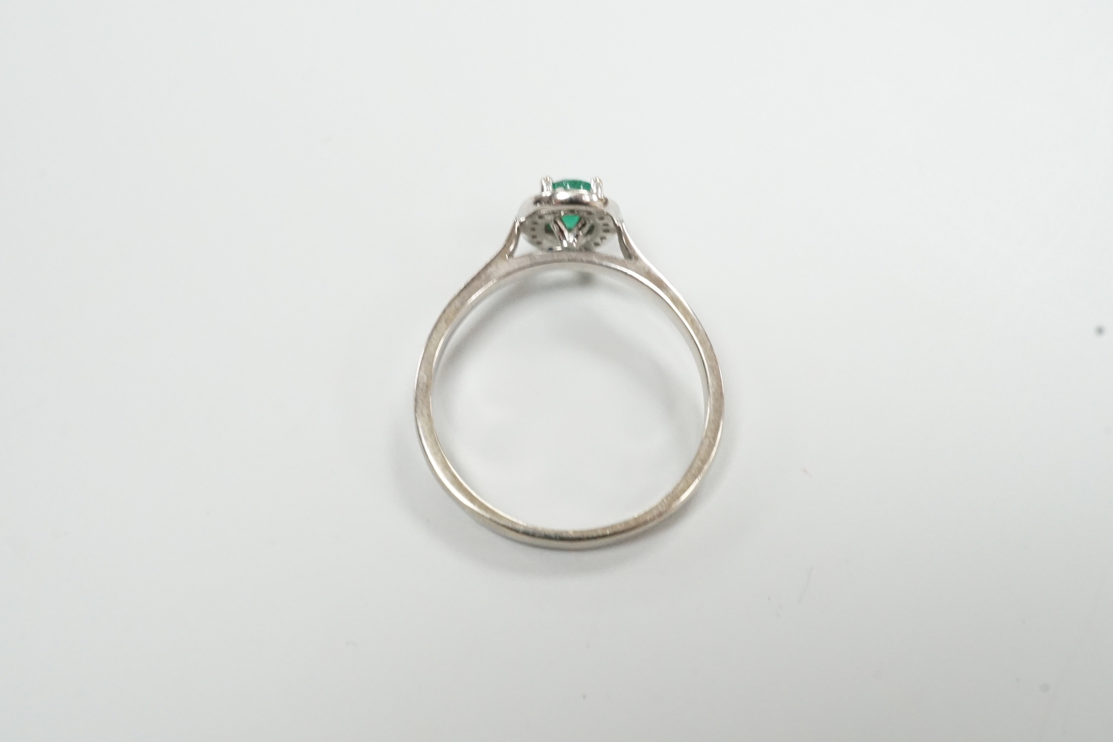 A modern 18ct white gold, emerald and diamond set oval cluster ring, size S, gross weight 3 grams.